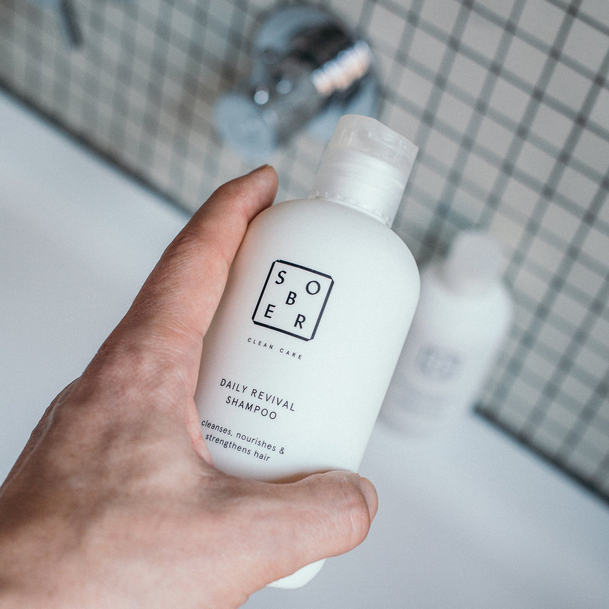 Hand hält Daily Revival Shampoo im Badezimmer